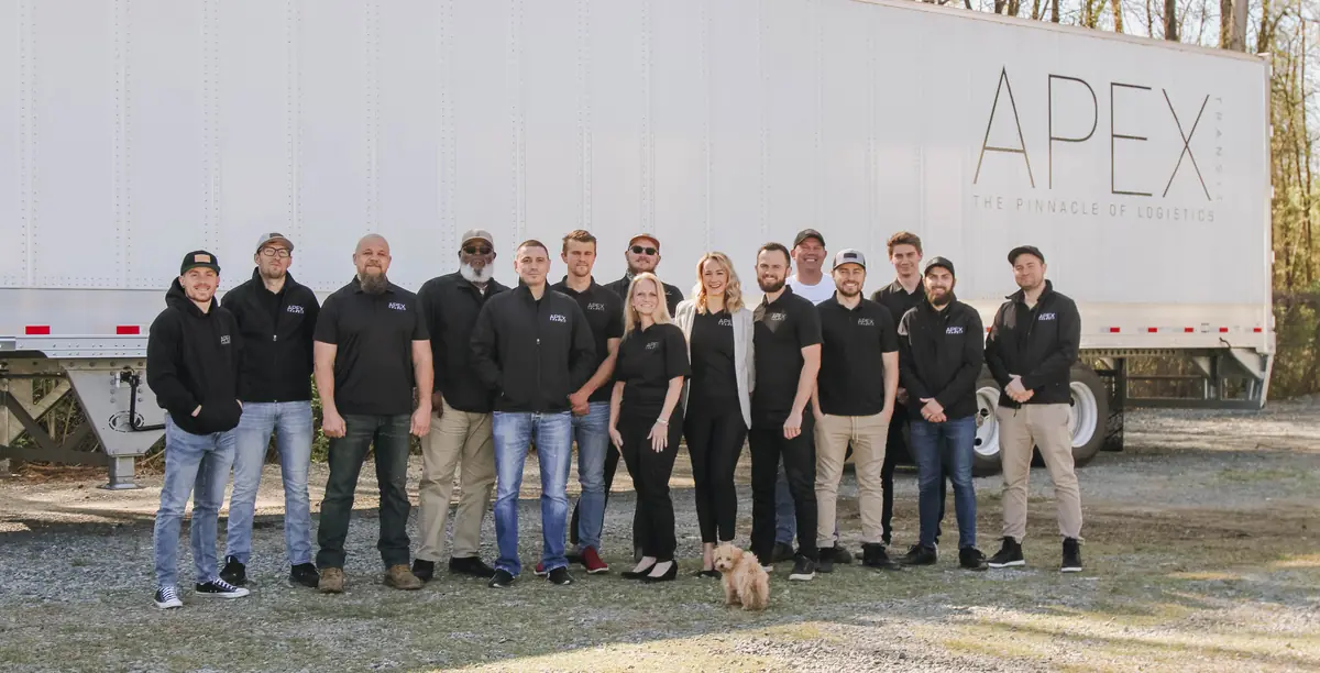 A group of Apex team members, and a small dog, standing in front of a white Apex trailer.